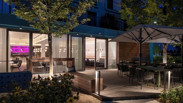 A modern outdoor patio area with a wooden deck, seating, and a covered dining area. - Hotel Le Parc (Wiener Neustadt)