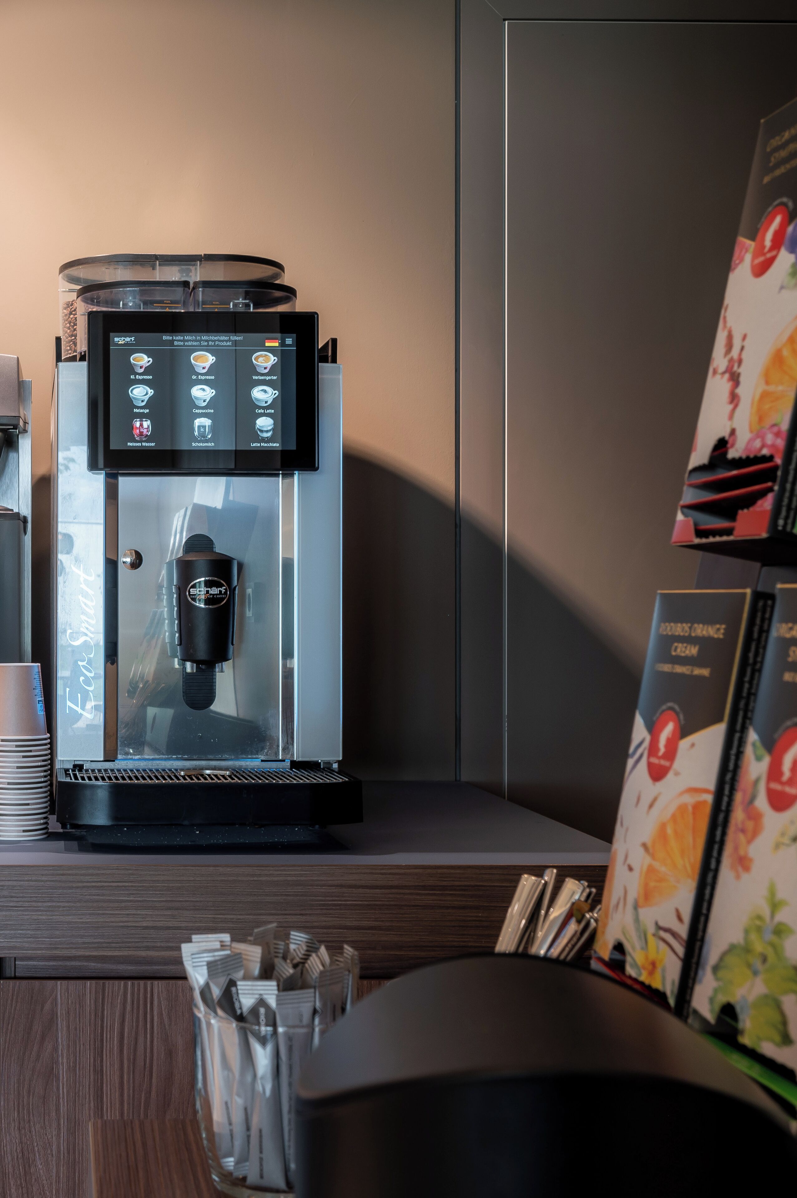A coffee machine with a digital display, a glass enclosure, and a coffee cup holder.