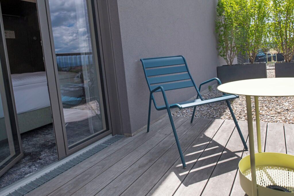 A room with a sliding glass door leading to a balcony, a blue chair, and a small round table.