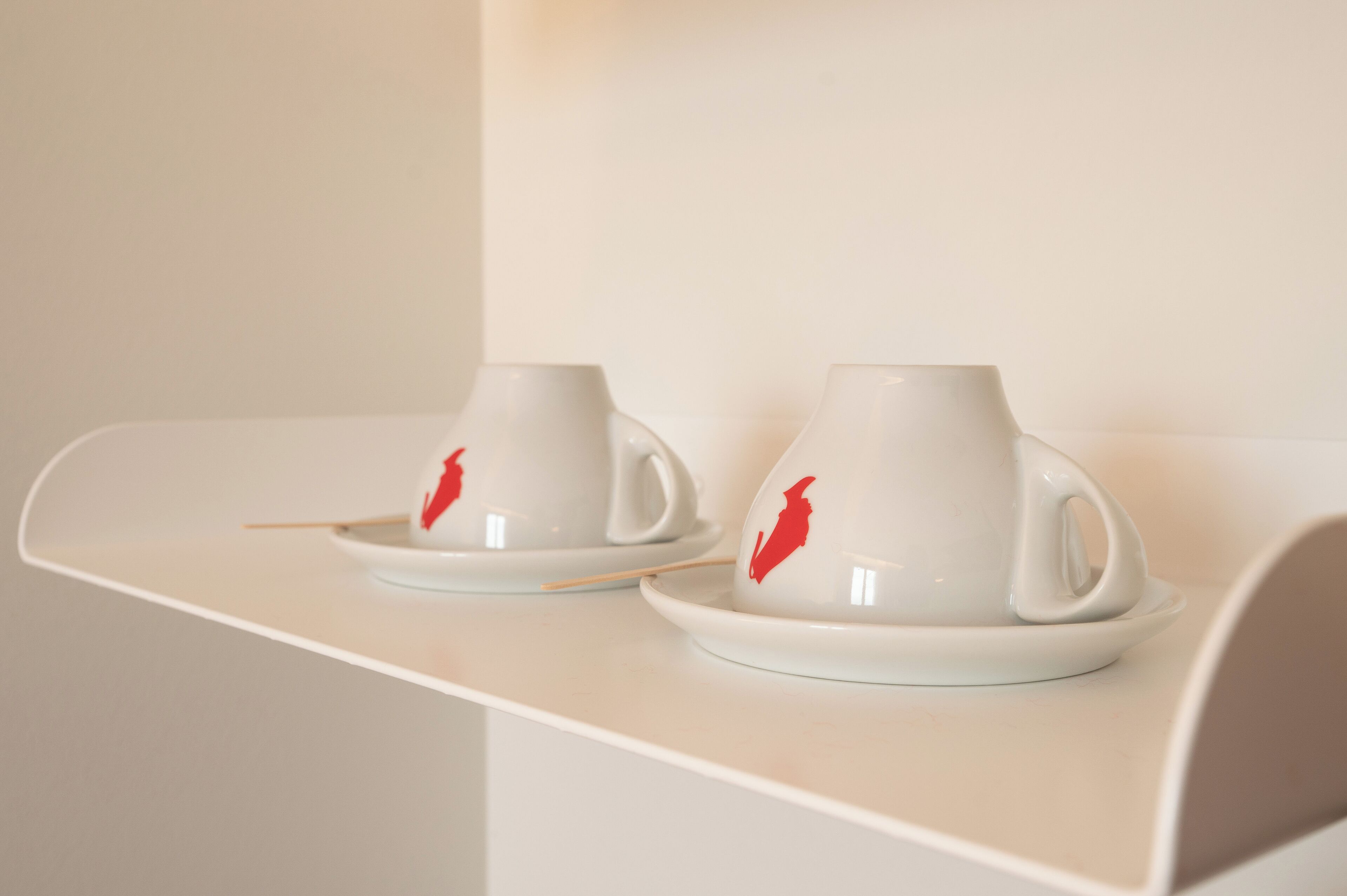 Twee witte bekers met rode patronen op een witte ondergrond.