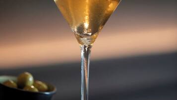 Una copa de martini con aceitunas en el borde y una pajita, sobre una superficie de madera con un fondo desenfocado.