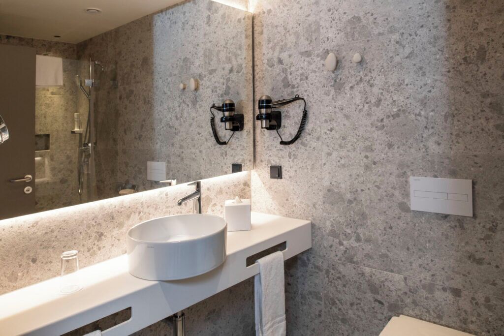 A modern bathroom with a large mirror, a round sink, and a shower.
