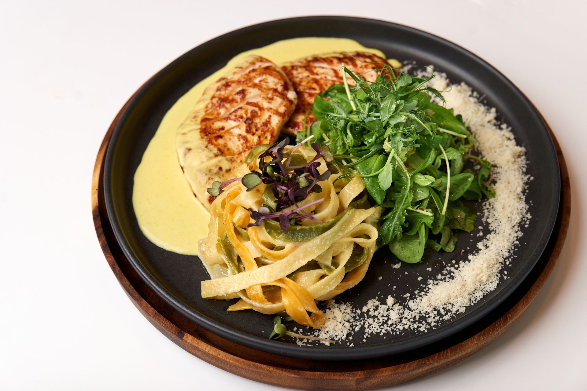Un plato de pasta, vegetales verdes y un trozo de carne, posiblemente pollo, sobre una tabla de madera.