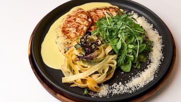 Un plato de pasta, vegetales verdes y un trozo de carne, posiblemente pollo, sobre una tabla de madera.