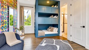 Una habitación con sofá, una litera azul, un tapete estampado y una ventana con cortinas.