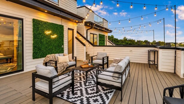 Una terraza al aire libre con un sofá, sillas, una mesa de centro, luces colgantes y una escalera.