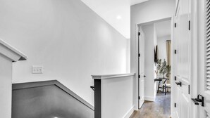 Un pasillo moderno con una escalera, paredes blancas y suelo de madera.