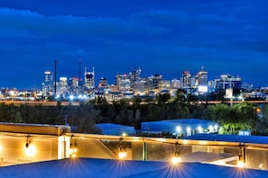 A city skyline at night with illuminated buildings, a bridge, and a parking area with tents.