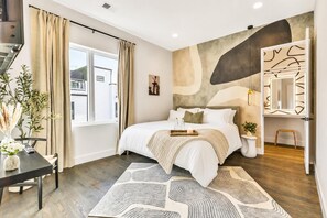 A modern bedroom with a large bed, a bedside table with a vase, a window with curtains, and a wall with abstract art. - Fall in Nashville: hot tub, game room house sleeps 12 near downtown (Nashville)