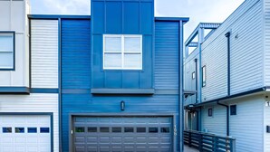 A modern two-story house with a blue exterior, a central garage, and a small balcony. - Fall Nashville weekend house with hot tub, mini golf & game room, sleeps 12 (Nashville)