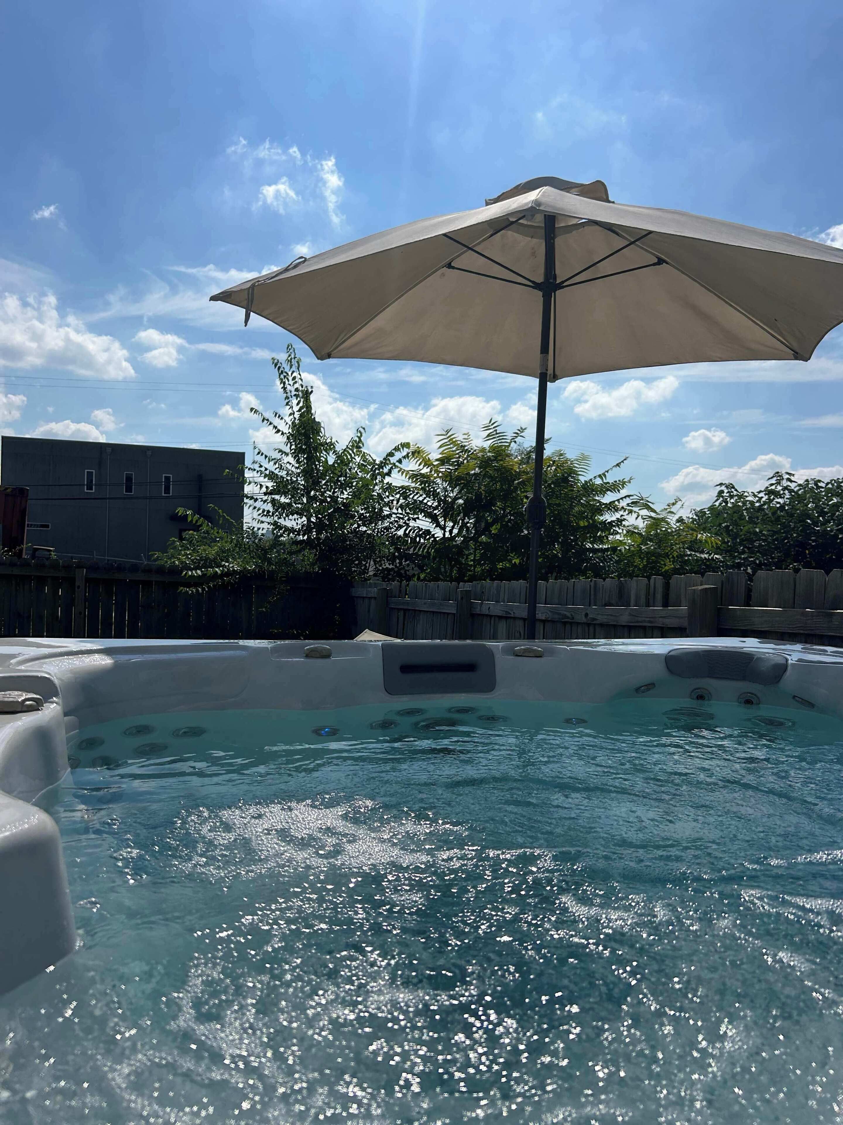 A hot tub area with a large umbrella, surrounded by trees and a wooden fence.