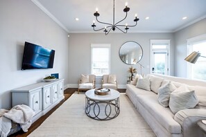 A modern living room with a large flat-screen TV, a round coffee table, a sofa, and a chandelier. - Fall getaway near Nashville: hot tub, game room, disco party room, sleeps 12 (Nashville)