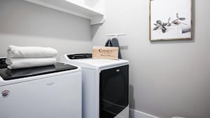 A laundry area with a white washing machine, a dryer, and a folded towel on the dryer. A framed picture of flowers hangs on the wall. - Fall Nashville weekend house with hot tub, mini golf & game room, sleeps 12 (Nashville)