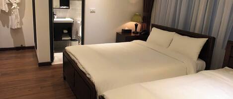 A hotel room with two beds, a bathroom with a mirror, and a wooden floor.