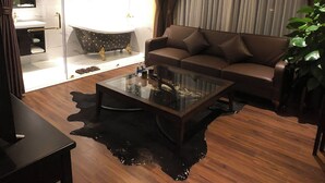 Ett modernt vardagsrum med ett glasbord, en brun soffa, en takfläkt och en skjutdörr i glas som leder till ett badrum.