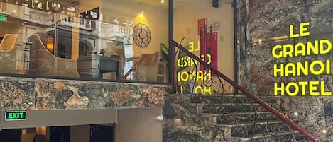 Un vestíbulo de hotel con una escalera de mármol, un candelabro y un letrero que dice "LE GRAND HANOH HOTEL".