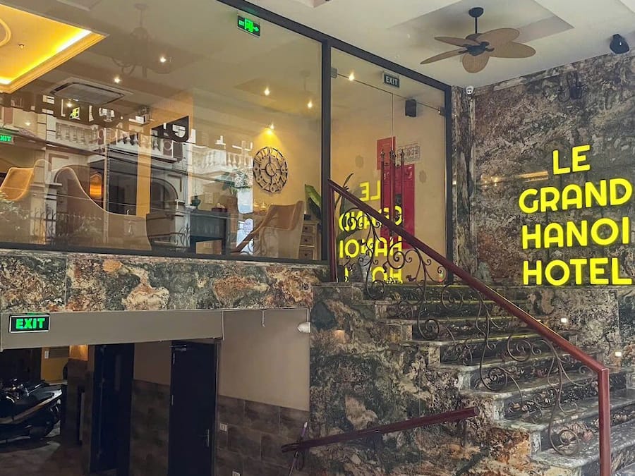 A hotel lobby with a marble staircase, a chandelier, and a sign reading "LE GRAND HANOH HOTEL".
