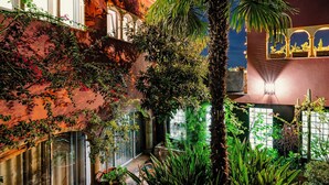 A courtyard with lush greenery, a palm tree, and a building with arched windows and a mural.