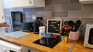 A kitchen with a washing machine, a coffee maker, a kettle, a sign saying "WELCOME ENJOY YOUR STAY", and a flower vase.