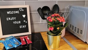 A kitchen counter with a black induction cooktop, a sign reading "WELCOME ENJOY YOUR STAY", and a potted plant with pink flowers.