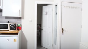A kitchen with a microwave, a coffee maker, and a small refrigerator. There is a door leading to a hallway with a coat rack.