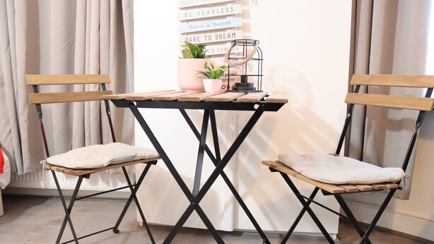 A room with a wooden-framed table and two chairs, a potted plant, and motivational signs on the wall.