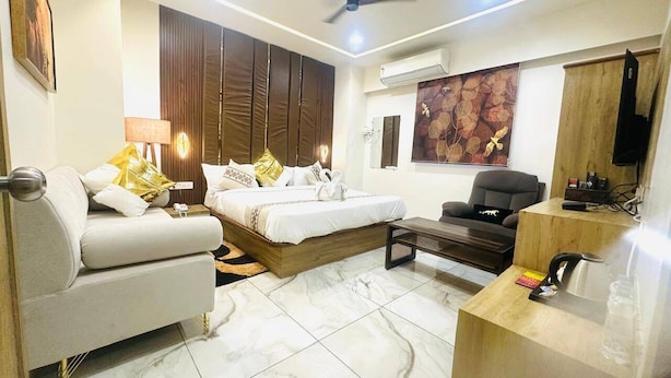 A modern hotel room with a bed, sofa, desk, and a ceiling fan. - Hotel Kings Residency (Ahmedabad)