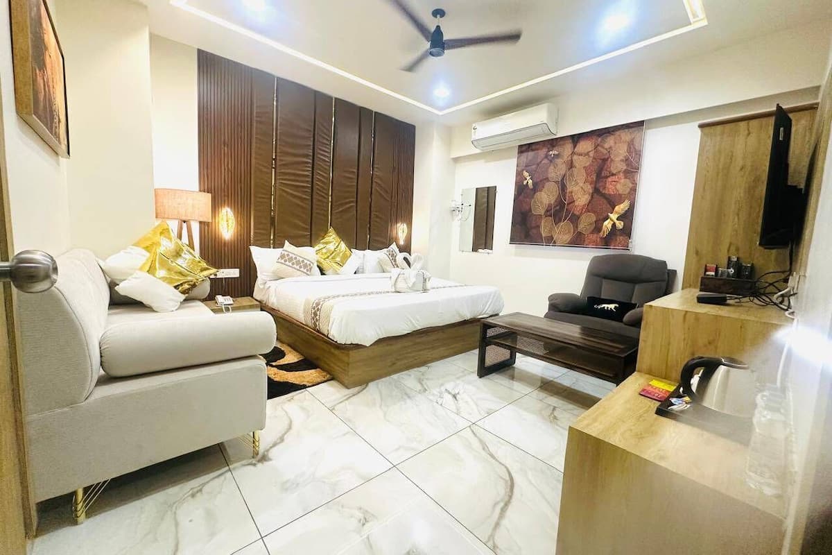 A modern hotel room with a bed, sofa, desk, and a ceiling fan.