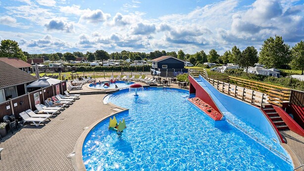 Una grande piscina con uno scivolo, sdraio e un'area ombreggiata con ombrelloni.