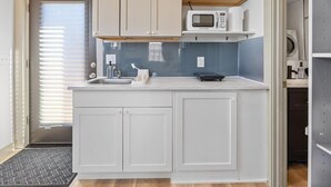 A compact kitchen with white cabinets, a microwave, and a sink. - Cityview Cottage (Indianapolis)
