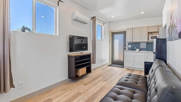 A modern living room with a sofa, a TV, and a kitchen area in the background. - Cityview Cottage (Indianapolis)