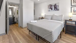 A bedroom with a bed, bedside tables, a mirror, and a door leading to a bathroom. - Cityview Cottage (Indianapolis)