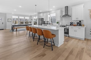 A modern kitchen with a central island, bar stools, white cabinetry, and a stainless steel range hood.