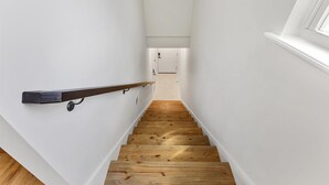 Uma escada estreita com degraus de madeira e um corrimão escuro, que leva a uma porta no topo.