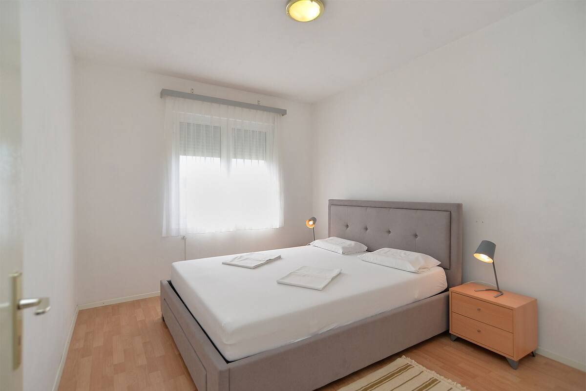 A bedroom with a bed, bedside tables, a window with curtains, and a light fixture.