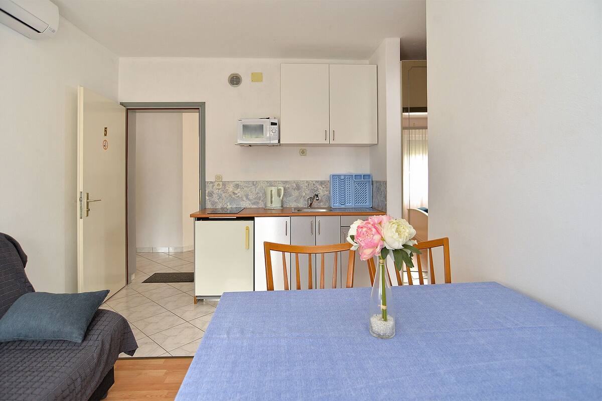 A compact kitchen with white cabinets, a microwave, and a sink. There is a dining table with a vase of flowers.