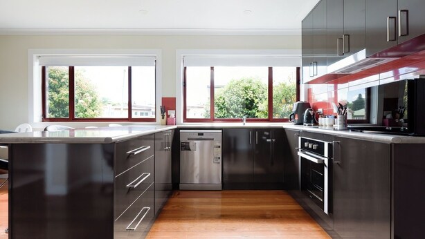 A modern kitchen with dark cabinetry, stainless steel appliances, and large windows offering views of greenery. - Spacious 3-Bed, Mins from City Centre (Newstead)