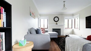A modern living room with a grey sofa, a small round wooden side table, a fireplace, and a bookshelf filled with books. - Spacious 3-Bed, Mins from City Centre (Newstead)