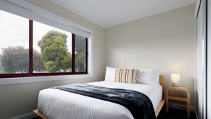 A hotel room with a large bed, a nightstand, a lamp, and a window with a view of trees. - Spacious 3-Bed, Mins from City Centre (Newstead)