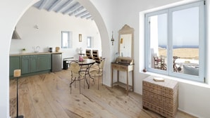 A spacious kitchen with an archway, a dining area with chairs, a wooden table, and a large window with a view of the beach.