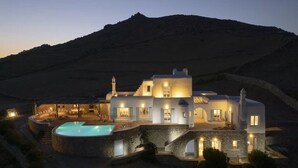 A modern villa with a swimming pool, stone architecture, and multiple rooms with exterior lighting.
