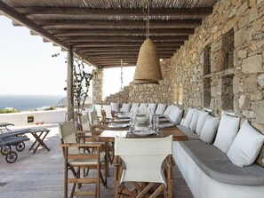 An outdoor dining area with stone walls, wooden furniture, and a view of the sea. - Villa With Panoramic sea Views (Mykonos)