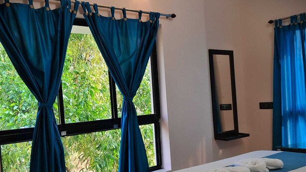 Een hotelkamer met een bed, een raam met gordijnen, een spiegel en uitzicht op groen.