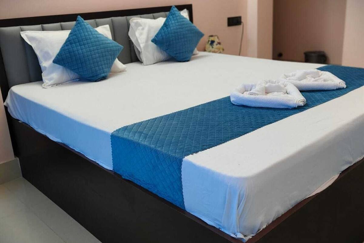 A neatly made bed with blue and white bedding, a dark headboard, and a small nightstand with a lamp.