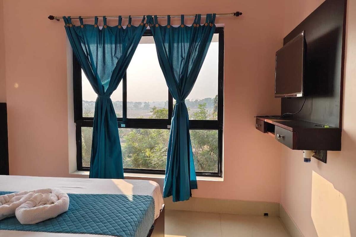 A bedroom with a bed, a TV mounted on the wall, and a window with curtains.