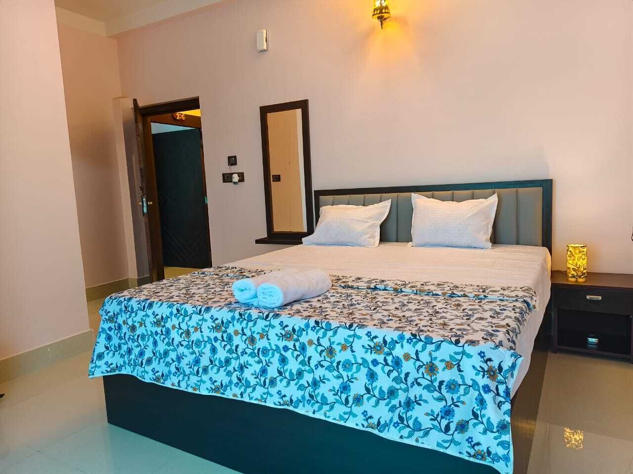Una cama bien hecha con una colcha estampada con motivos florales, una lámpara de noche y una mesita.