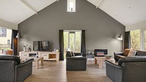 A spacious living room with a high ceiling, a fireplace, a television, and leather sofas. - Summio Waterpark De Bloemert (Midlaren)