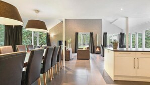A modern kitchen with a large island, dining area with chairs, a fireplace, and large windows with curtains. - Summio Waterpark De Bloemert (Midlaren)