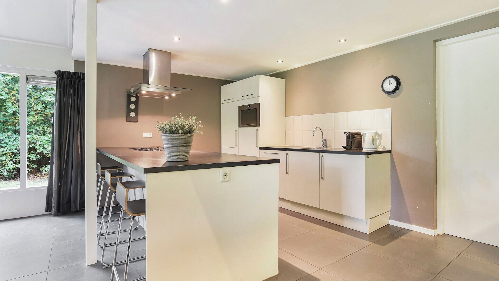 A modern kitchen with a central island, built-in oven, and a clock on the wall.