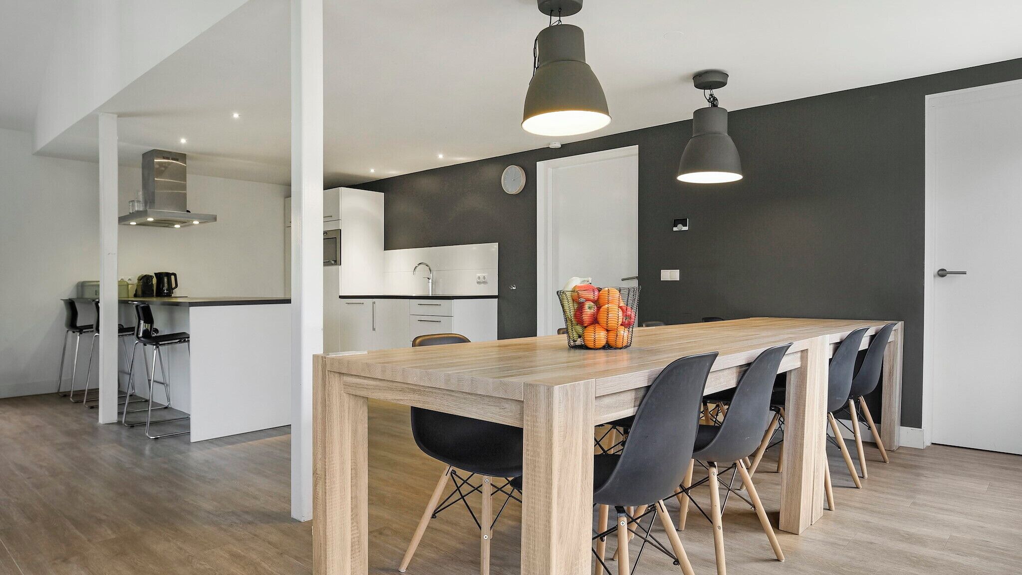 A modern kitchen with a wooden dining table, black chairs, and pendant lights.